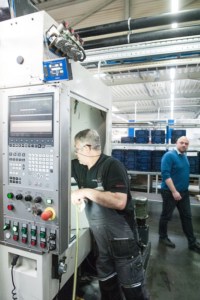Ein Produktionsmitarbeiter beim Säubern der Fräsmaschine, in die das Inline-Messsystem ATC eingebaut ist. Oben links das blaue Kästchen ist das GUI des ATC
